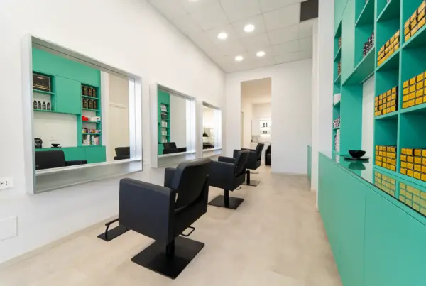 Postazione di styling con poltrona nera davanti a mobili verde acqua con prodotti per il colore