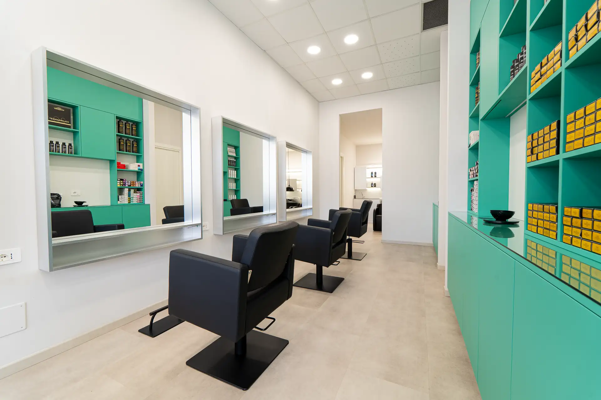 Postazione di styling con poltrona nera davanti a mobili verde acqua con prodotti per il colore