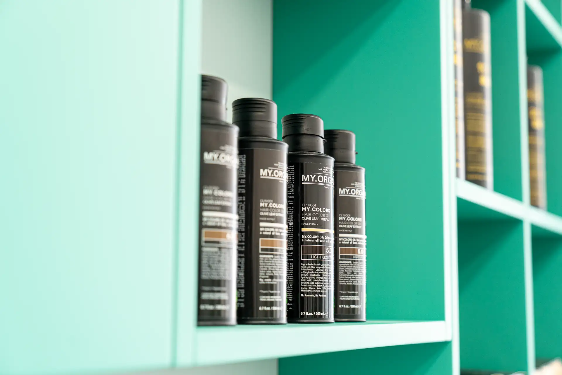 Flaconi neri di prodotti colore My.Organics su uno scaffale verde acqua del salone