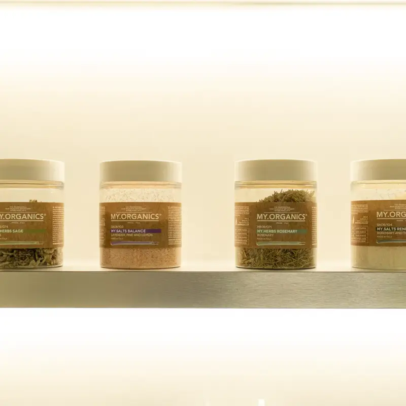Quattro barattoli My.Organics con erbe e sali su una mensola illuminata della cabina Head Spa