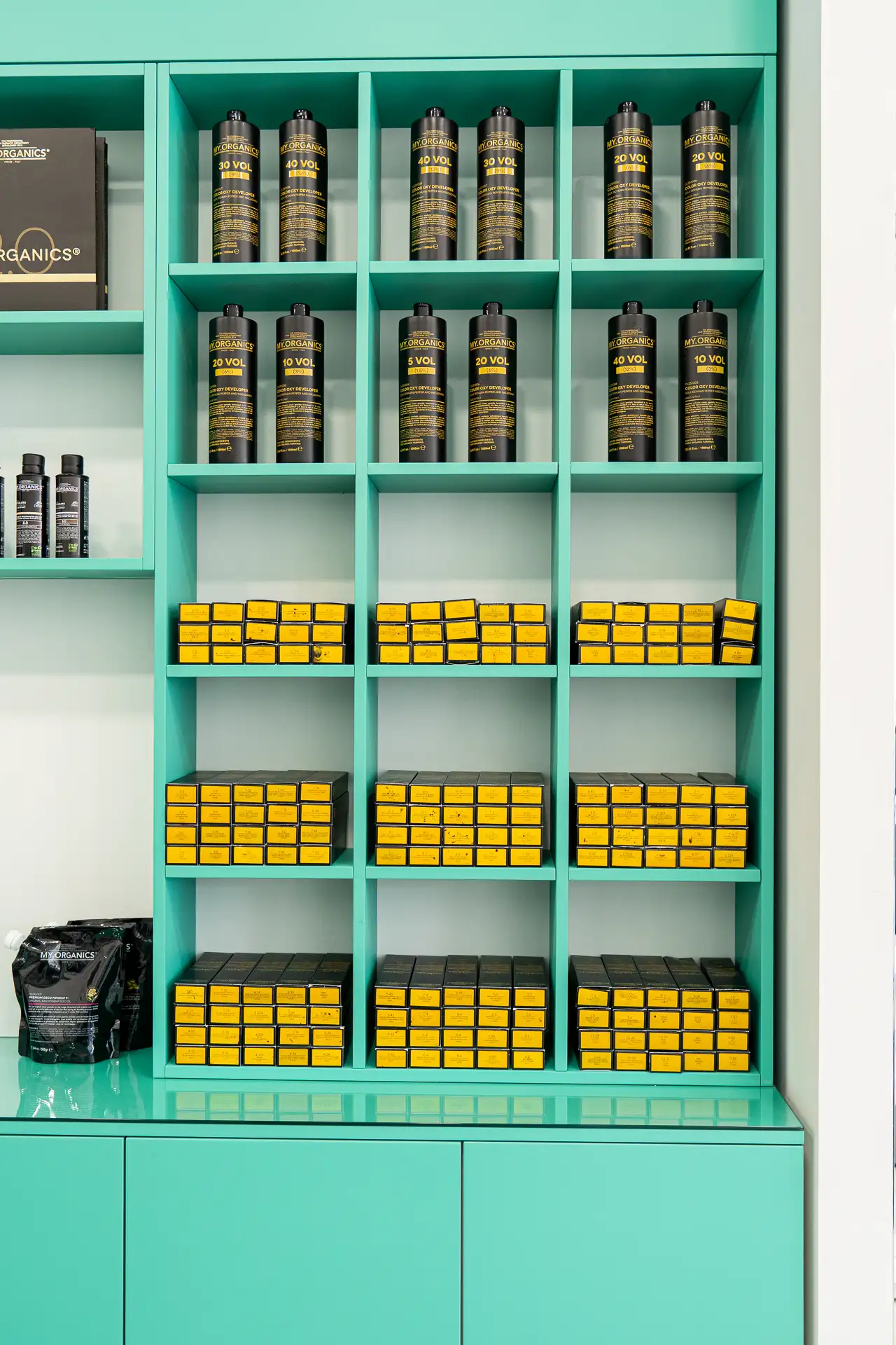 Scaffalatura verde acqua con flaconi neri e confezioni gialle di prodotti per il colore dei capelli