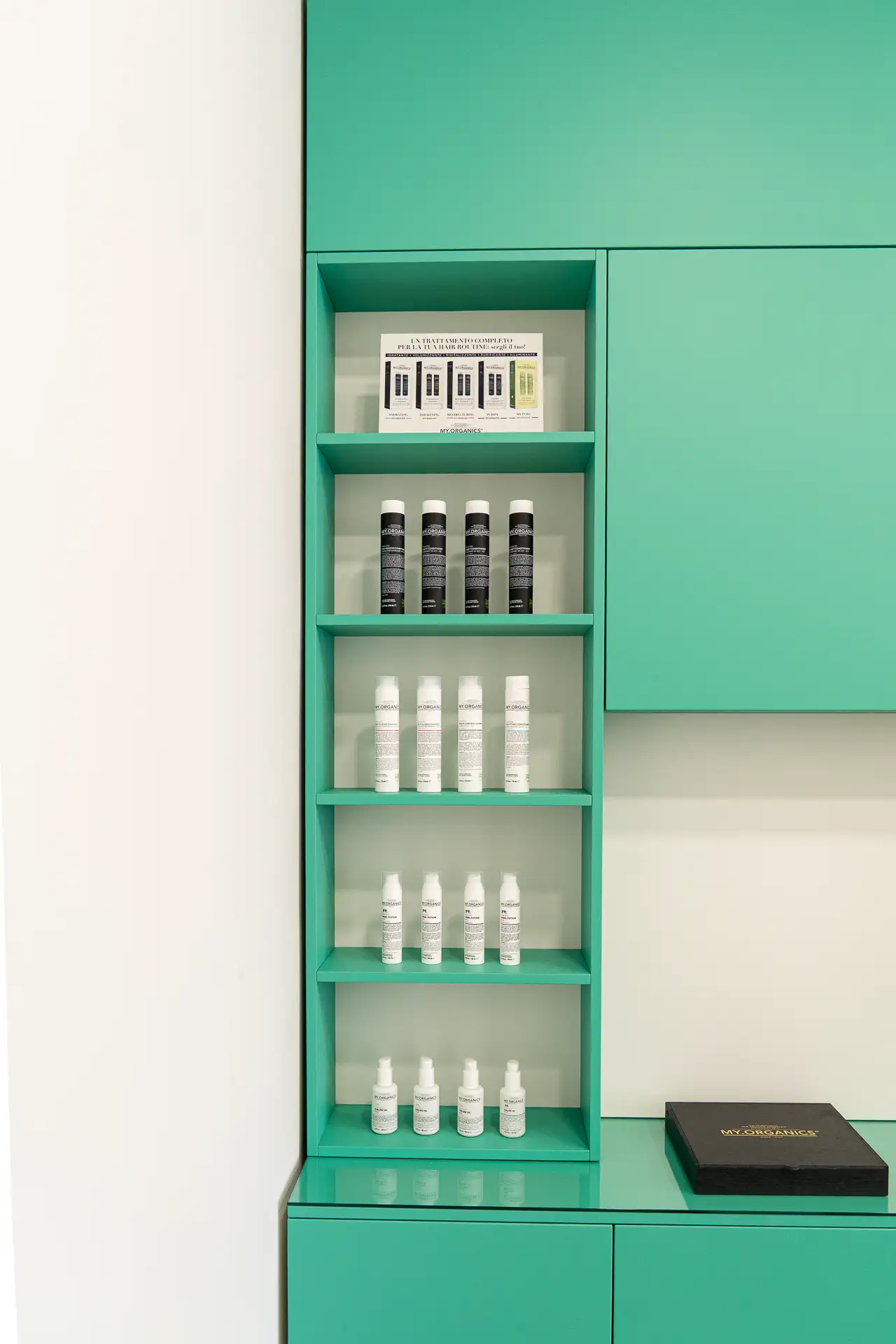 Scaffale verde acqua con flaconi bianchi e neri di prodotti professionali per capelli